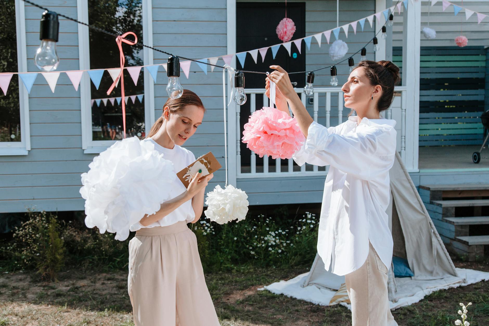 Dwie kobiety dekorują ogród lampkami i pomponami na przyjęcie